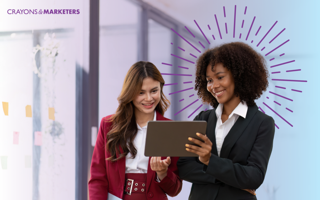 Two women in business attire collaborate while holding a tablet computer, discussing work-related content.